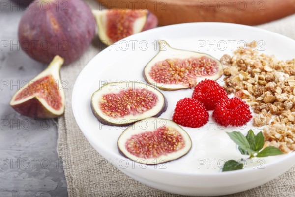 Yoghurt with raspberry, granola and figs in white plate on a gray concrete background and linen