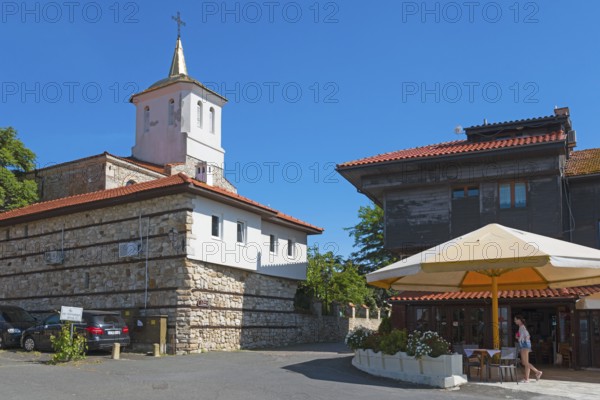 Historic church under clear blue sky next to urban buildings with people and parked cars, Orthodox