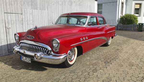 A shiny red classic car with chrome details parked in front of a white garage door, classic car,