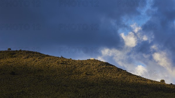 Sunlight and shadow play across a grassy hill under a dramatic sky with dense clouds, Lefka Ori,