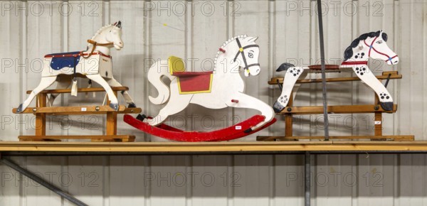 Three wooden rocking horses in a line on display in auction room, UK