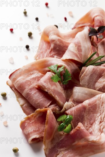 Raw bacon, sliced, with micro greenery and spices, on a white background, close-up