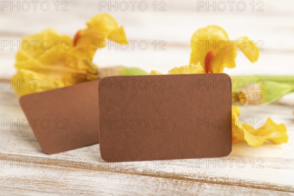Brown business card with iris yellow flowers on white wooden background. side view, copy space,