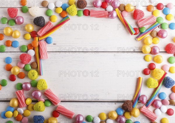 Colorful frame of multicolored candies on white wooden background. Circle copy space, top view,