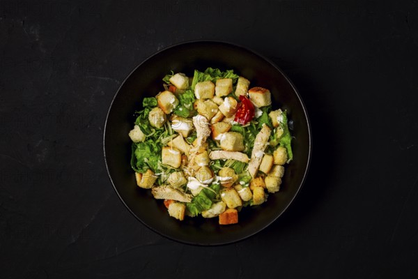 Fresh traditional Caesar salad, with chicken, on a black background, Top view, dark background,