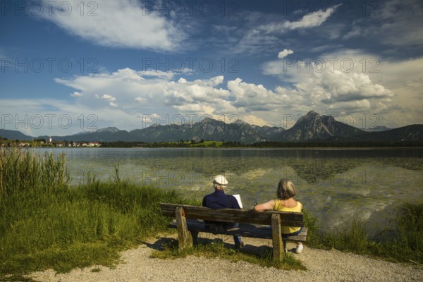 Elderly couple, pensioner, park bench, Hopfensee, near Fuessen, behind them the Ammergau Alps,