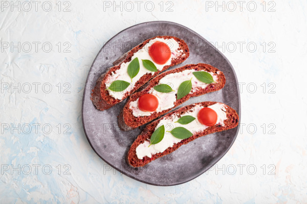Red beet bread sandwiches with cream cheese and tomatoes on white concrete background. top view,