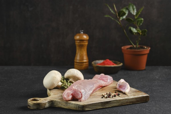 Raw rabbit tenderloin on a wooden cutting board beside fresh mushrooms and an assortment of spices.