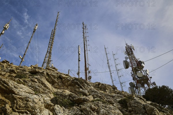 Several radio masts and antennas towering into the cloudy sky on a rocky hill, mountain top,