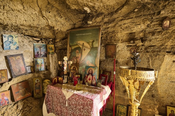 Interior view of a rock cave with an altar decorated with numerous religious pictures and icons, as