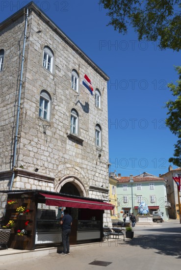 Tall stone building with characteristic windows and a flag, surrounded by trees and a clear blue