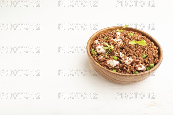 Quinoa porridge with green pea and chicken in wooden bowl on a white wooden background. Side view,