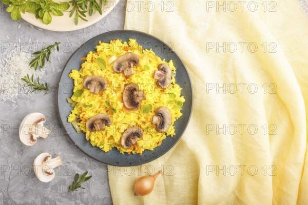 Yellow fried rice with champignons mushrooms, turmeric and oregano on blue ceramic plate on a gray