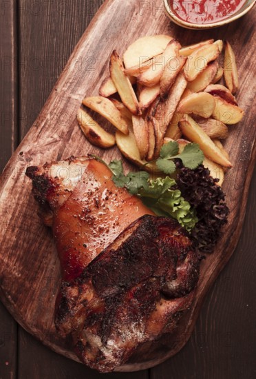 Pork knuckle, in soy-honey sauce, with fried potatoes, on a wooden chopping board, homemade, no
