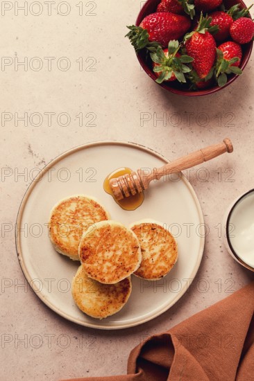 Cottage cheese pancakes with white sauce and strawberries, on a beige table, top view, selective