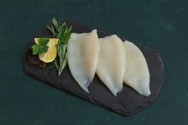 Fresh squid body, raw, three carcasses, top view, on black slate, no people