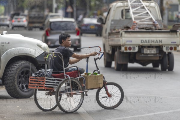 Man with an amputated leg on a hand-propelled tricycle, road traffic in Vientiane, Laos, Asia
