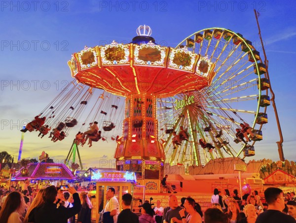 The colourfully illuminated Wellenflug chain carousel and the Ferris wheel in the evening, Cranger