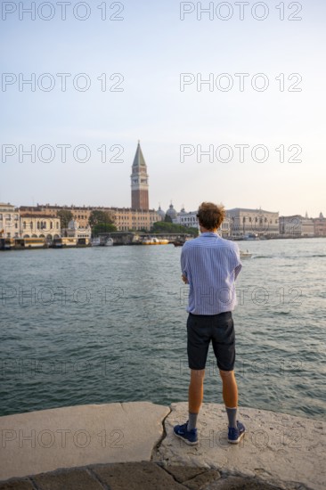 Young man in striped shirt and shorts on the banks of the Grand Canal, behind Campanile, Venice,