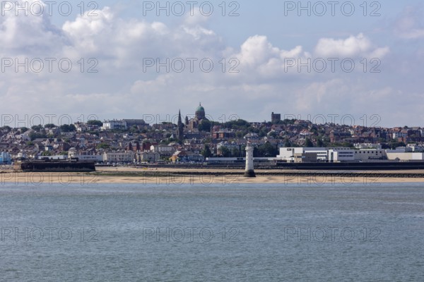 Coastal view with a strip of beach and urban background with prominent tower in clear sky,