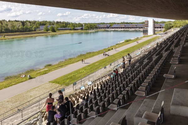 Perspective from grandstands on a lake with sporting activities and green surroundings,