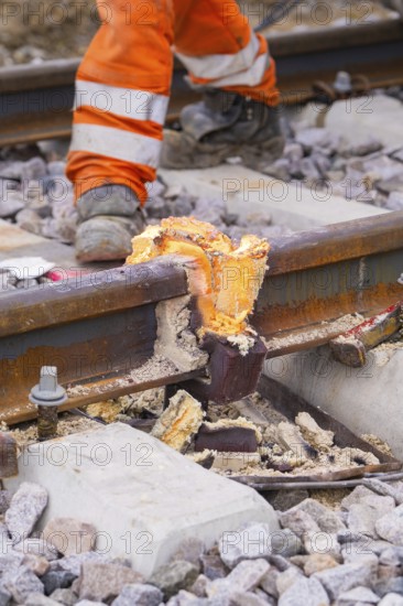 Close-up of a damaged section of track with a construction worker dressed in orange in the