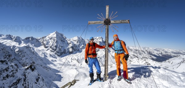 Two ski tourers at the summit cross on the summit of the Madritschspitze, mountain panorama with