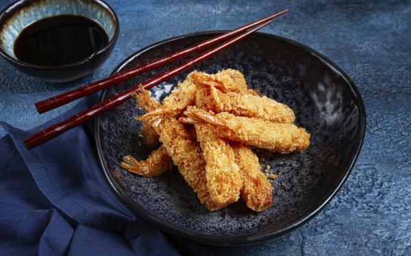 Shrimp in tempura, deep fried, on a black plate, with soy sauce, close-up, top view, no people