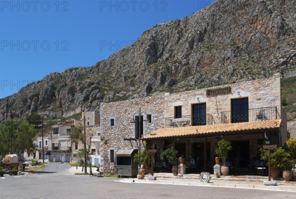 A Mediterranean village with stone buildings in front of a rocky mountain landscape under a clear