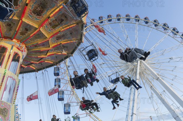 People swinging on a carousel in front of a Ferris wheel in sunny weather at a funfair, Europa Rad,