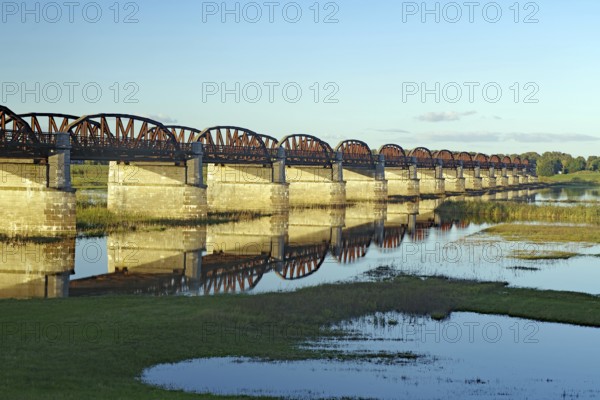 Long, arched stone bridge reflected in the calm river water under a clear sky, autumn, Elbe,