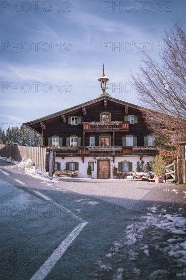 Traditional Bavarian country house on a snow-covered road under a clear blue sky, Der Bergdoktor