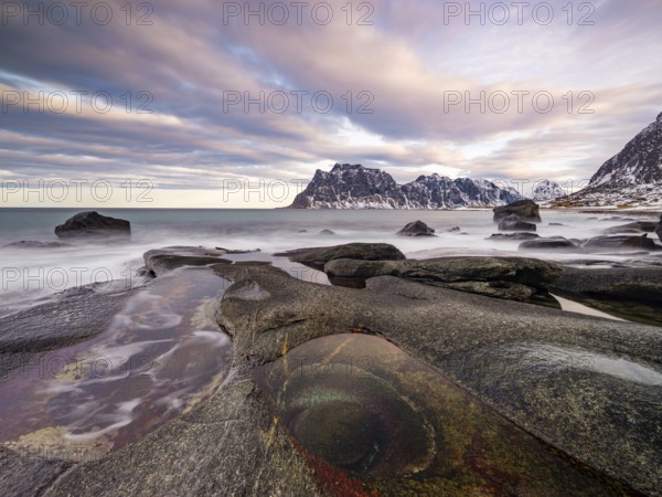 Rocks at Utakleiv beach with rock formation Eye of Utakleiv, or Dragon's Eye, in a dramatic cloudy