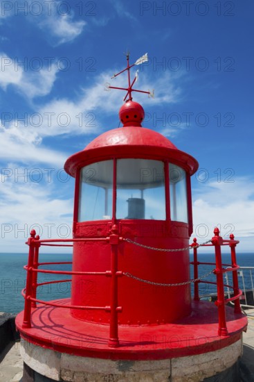 Red lighthouse with round roof on a coastal platform, blue sky and sea in the background, Fort São