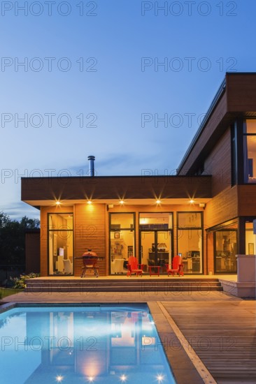 Modern cube style home with stained horizontal wood cladding and in-ground swimming pool at dusk,