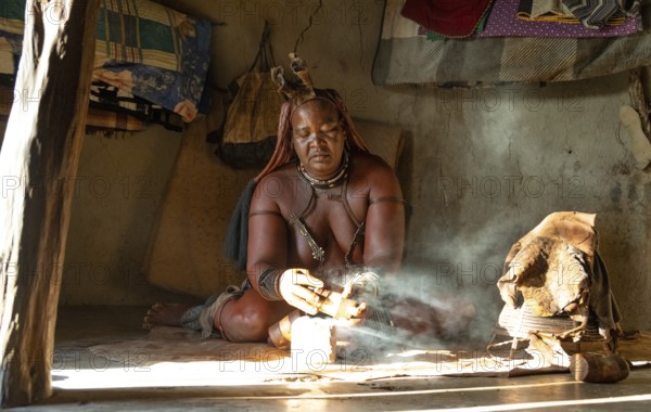 Traditional Himba woman prepares herbs for body care with smoke, Interior of the first woman's mud