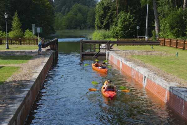 Two canoeists on a water canal under a small bridge in a wooded area, Sluza Perkuc, Perkuc lock,