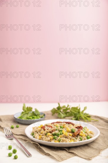 Quinoa porridge with green pea, corn and dried tomatoes on ceramic plate on a white and pastel pink