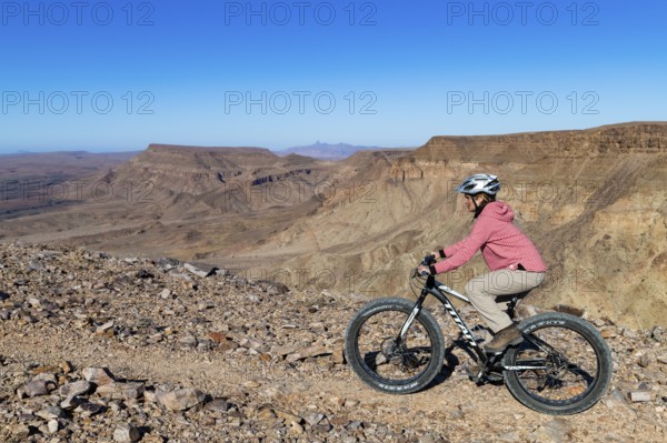 Woman riding a mountain bike, fatbike, on the edge of the abyss, behind the gorge landscape of the
