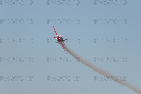 Red stunt aerobatic plane performing stunts in blue sky. Concept of speed, difficulty, precision,