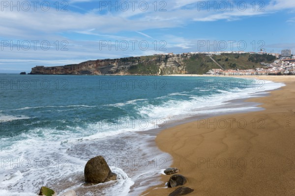 View of the beach coast of Nazaré with waves, sand and a picturesque hill in the background, Praia