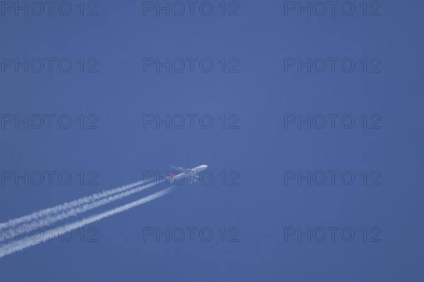Boeing 747 jumbo jet aircraft flying across a blue sky with a vapour trail or contrail behind,