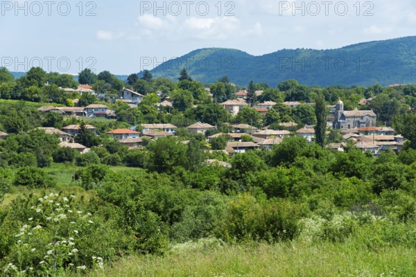 A quiet village surrounded by green hills and trees under a partly cloudy sky, Gagovo, Popovo,