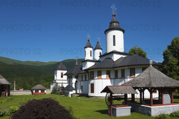 A peaceful Orthodox church with white walls and black roofs in front of a mountain, Cheia Romanian