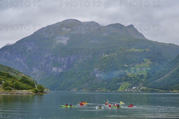 Several kayakers in a fjord surrounded by forested mountains and clouds, Geiranger, Geiranger