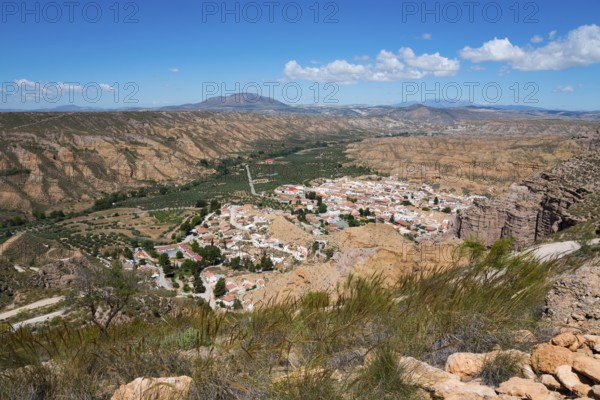 A village with white houses and red roofs, nestled in a dry, mountainous desert landscape under a
