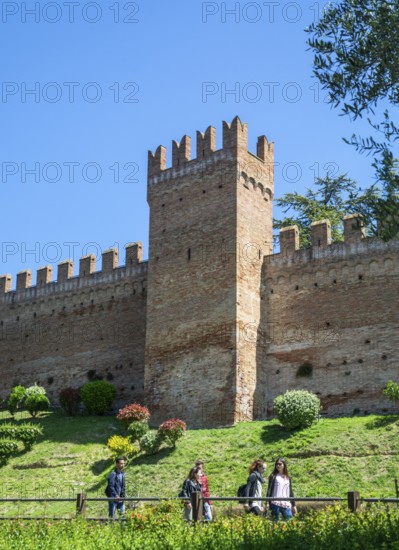 People walk in front of a tower on the defense wall of the medieval Gradara castle, Marche region,