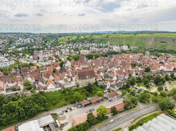 Urban settlement with tightly packed red roofs, surrounded by green hills and crossed by roads,