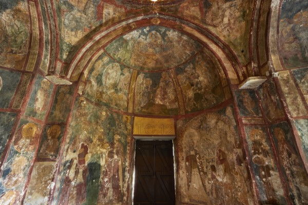 A church interior with frescoes on the walls, religious art and a large wooden door, Byzantine