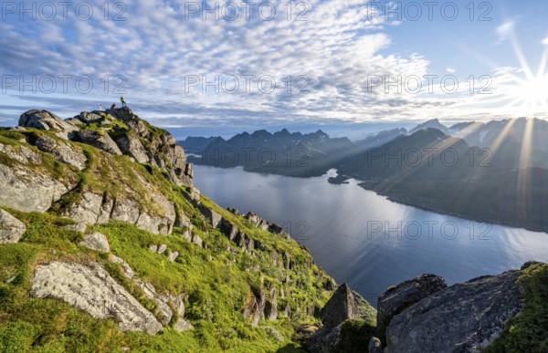 Mountaineer on the summit of Dronningsvarden or Stortinden, behind sea and fjord Umvågsundet,